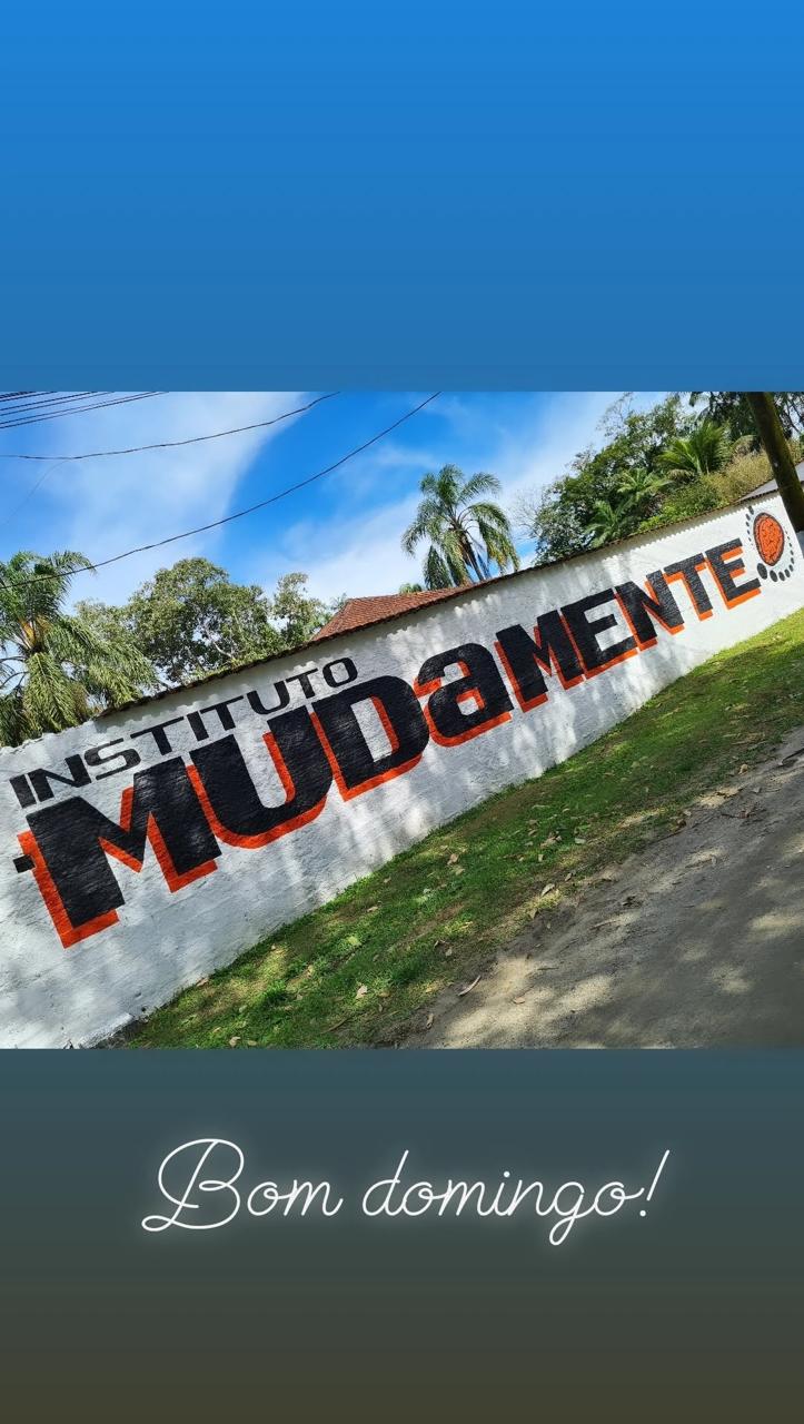 Registro vertical da fachada e do muro Muda Mente, com faixas de story e a mensagem Bom domingo.