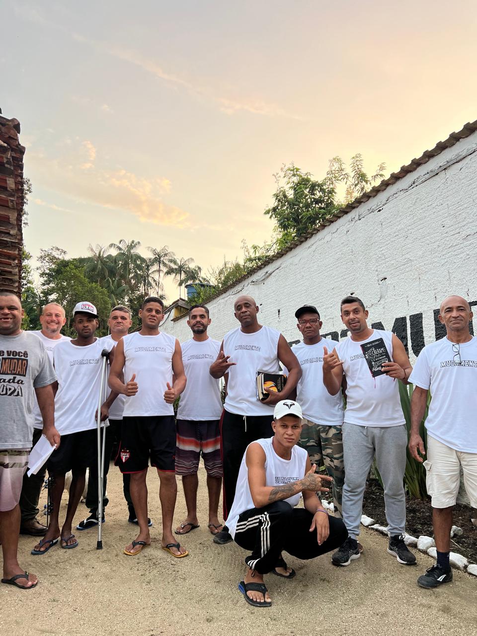 Grupo de pessoas reunido diante do muro do Instituto Muda Mente ao entardecer.