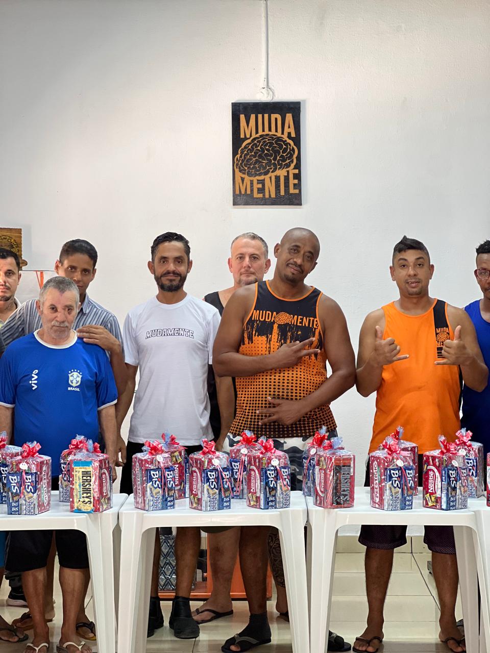 Grupo de pessoas em uma sala, atrás de uma mesa com copos e pequenos presentes.