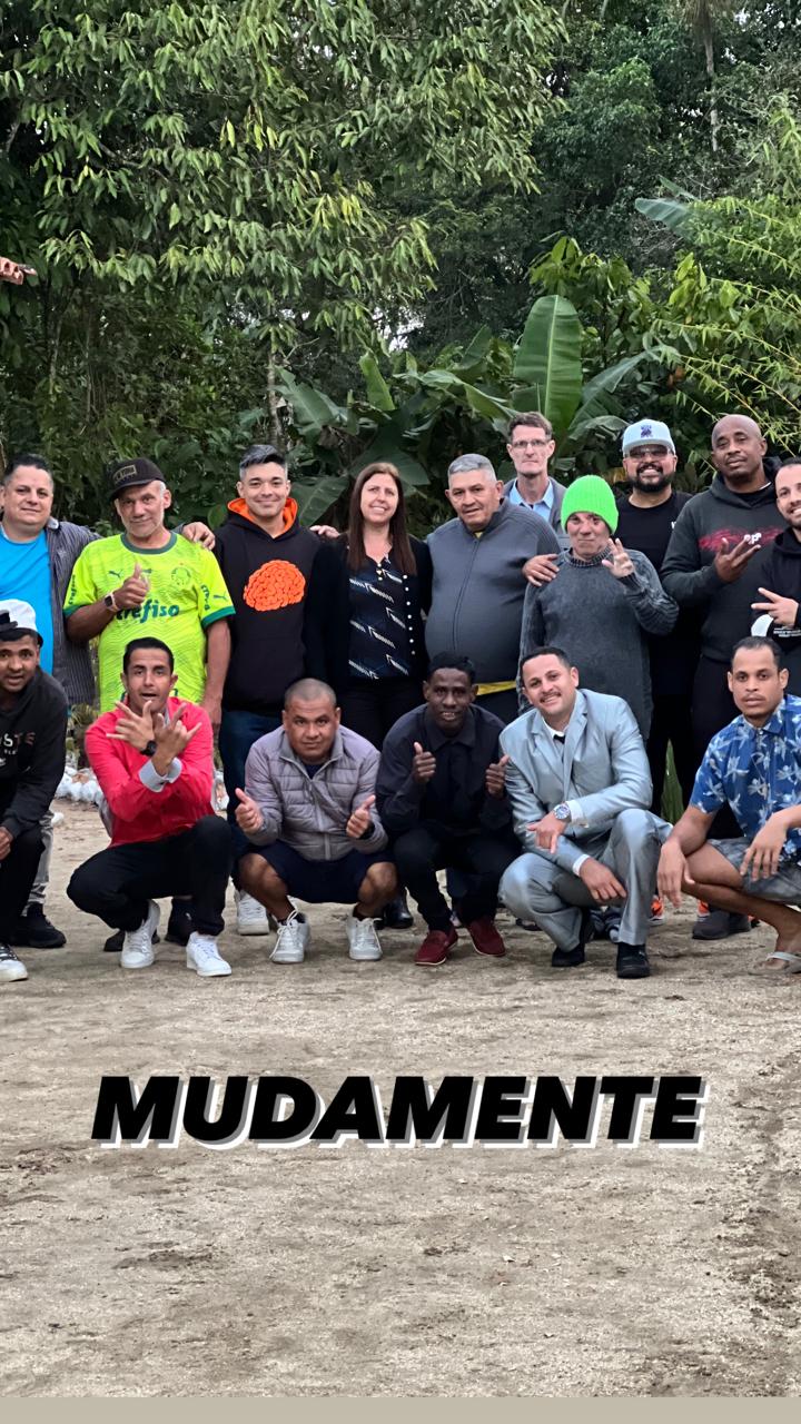 Grupo de pessoas posando em uma área externa arborizada, com a palavra Muda Mente na imagem.