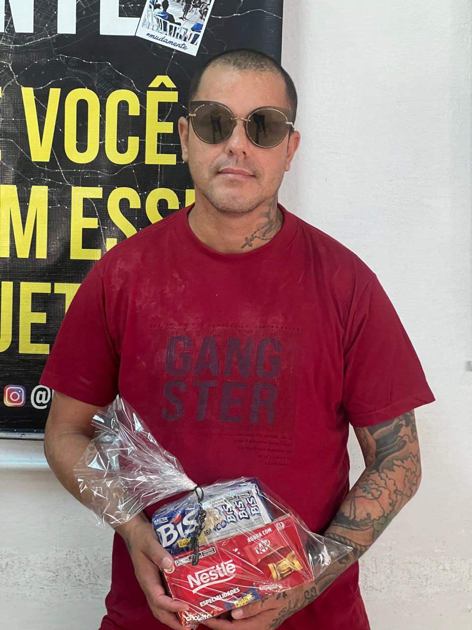 Homem segurando pequenos presentes diante de um painel de mensagens.
