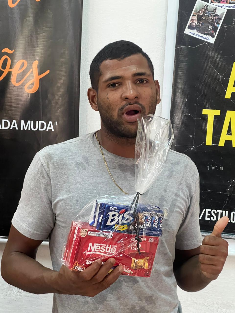 Homem segurando pequenos presentes diante de um painel de mensagens.