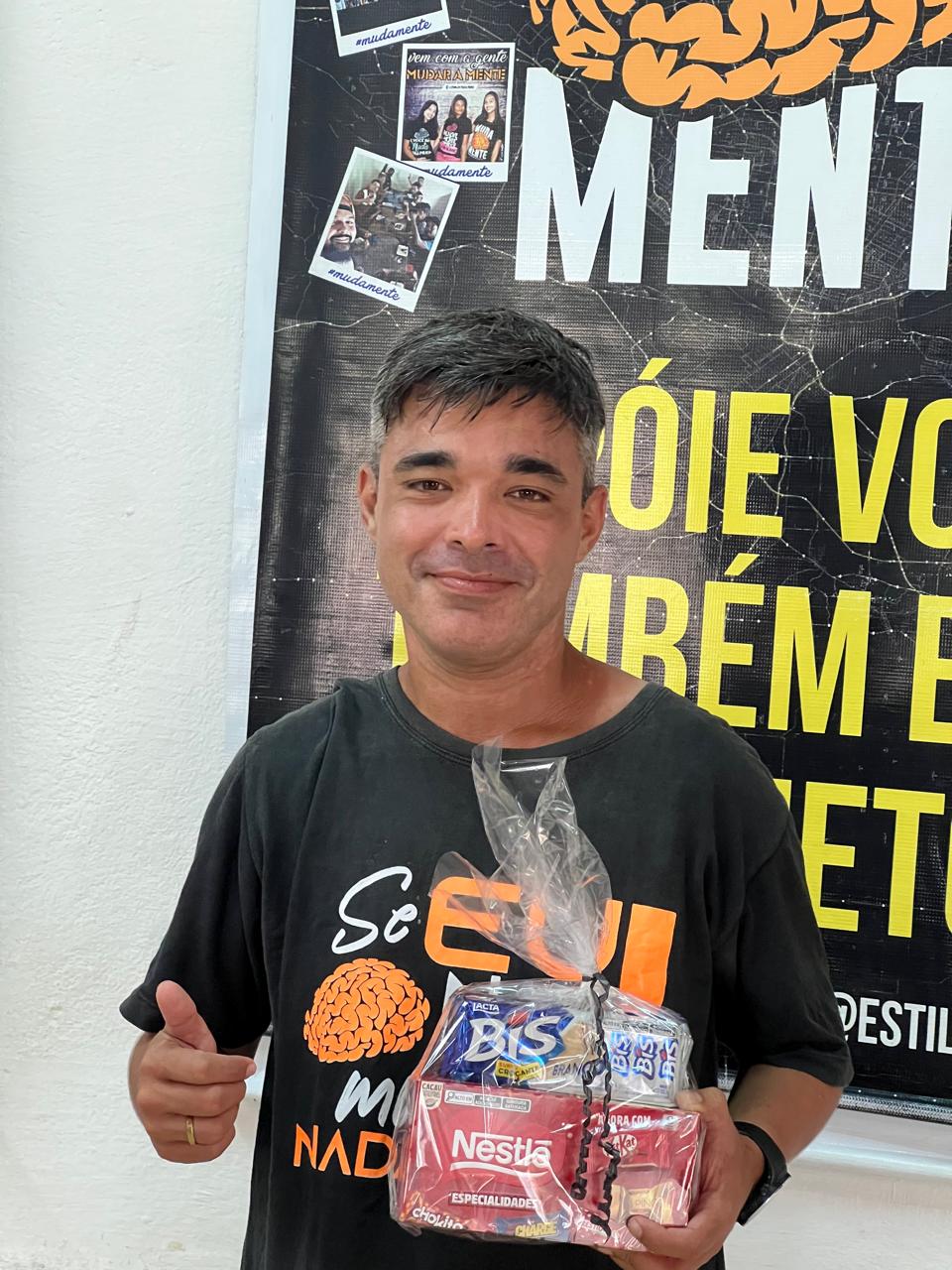 Homem sorrindo, segurando pequenos presentes e fazendo gesto positivo com a mão.